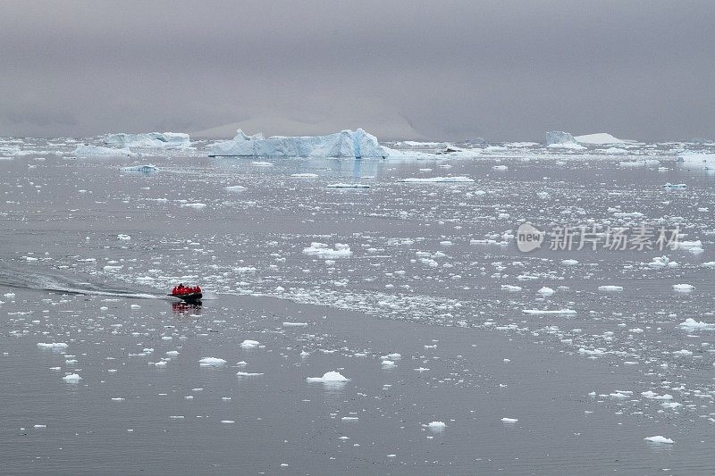 一艘Zodiac橡胶摩托艇载着来自探险游轮MV Sea Spirit (Poseidon Expeditions)的乘客在一片宽阔的浮冰上旅行，地平线上有更大的冰山